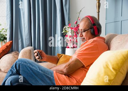 Indischer asiatischer alter Mann, der Kopfhörer benutzt, während er Musik hört Oder Filme auf einem Tablet-Computer oder Smartphone ansehen Stockfoto