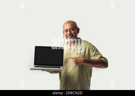 Indische asiatische ältere Erwachsene Mann oder Opa präsentiert leeren Laptop Bildschirm vor weißem Hintergrund Stockfoto