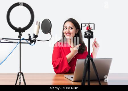 Hübsche Inderin spricht vor dem Mikrofon, während sie einen Videoblog für seine Abonnenten aufnimmt und dabei die Kamera anschaut Stockfoto