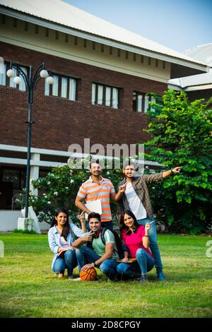 Fröhliche Gruppe von indischen asiatischen College-Studenten zeigt auf leer Im Stehen oder Sitzen auf dem College-Campus Stockfoto