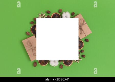 Leere Papierkarte mit Rahmen aus natürlichen Weihnachtsgeschenken und Dekorationen. Quadratisches Modell auf grünem Hintergrund. Stockfoto