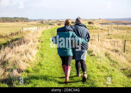 Mutter und Erwachsene Tochter, die gemeinsam am Fluss Ore, Suffolk, England, Großbritannien von hinten umarmen Stockfoto