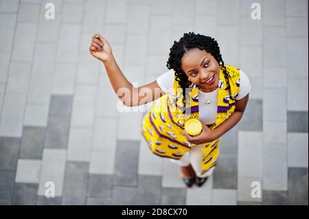 Blick von oben auf stilvolle afroamerikanische Frauen in gelber Jacke auf der Straße mit heißem Getränk in Einweg-Papierbecher gestellt. Stockfoto