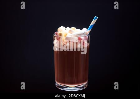 Ein Glas heiße Schokolade mit bunten Marshmallows und einem Trinkhalm auf schwarzem Hintergrund. Stockfoto