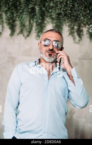 Porträt eines Mannes mittleren Alters mit Bart und Sonnenbrille im Gespräch am Telefon. Stockfoto