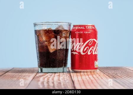 London, Vereinigtes Königreich - Oktober 29 2020: Eiskalte Dose von Coke sitzt neben einem vollen Glas Coca Cola auf einem Holztisch mit blauem Hintergrund Stockfoto