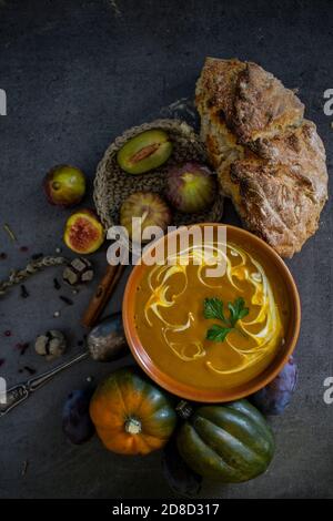 Herbstmenü. Draufsicht Foto von Schüssel mit Kürbissuppe, Edelsteinpfeifer, Rosmarin, Pfeffer, frisch gebackenem Brot und Silberlöffel. Dunkelgrauer Hintergrund. Stockfoto