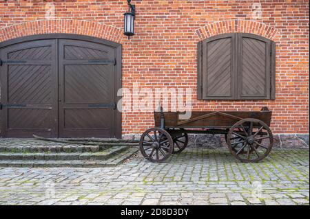 Alte Holzkarre mit Globulars auf dem Bürgersteig gegen die rote Backsteinmauer mit Toren, Fensterläden und einer Laterne, Kopierraum Stockfoto