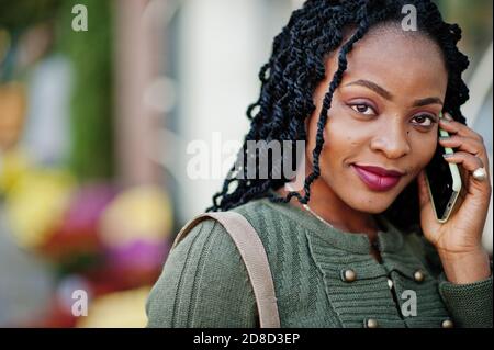 Stilvolle modische afroamerikanische Frauen in grünen Pullover und schwarzen Rock posiert Outdoor-Café mit Tasse Kaffee und sprechen auf Handy. Stockfoto