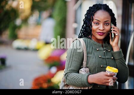 Stilvolle modische afroamerikanische Frauen in grünen Pullover und schwarzen Rock posiert Outdoor-Café mit Tasse Kaffee und sprechen auf Handy. Stockfoto