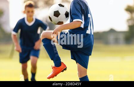 Kinder Fußballspieler jonglieren einen Ball auf den Knien. Kinder beim Fußballtraining im Freien. Junge im blauen Fußballtrikot jongliert mit einem Ball Stockfoto