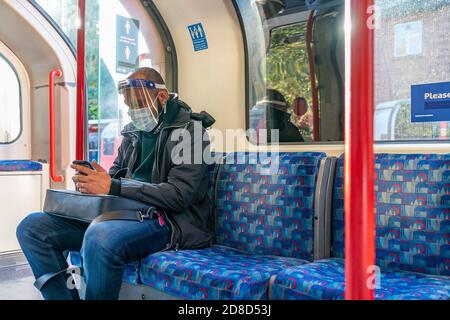 LONDON, ENGLAND - 23. OKTOBER 2020: Inder mit Gesichtsschutz und Mobiltelefon während der COVID-1 in der Londoner U-Bahn unterwegs Stockfoto
