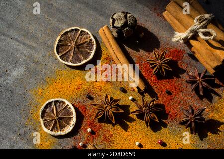 Gewürze auf einem Tisch. Kurkuma und Paprikapulver, Pfeffer, Anis Sterne und Zimtstangen auf dunkelgrauem texturiertem Hintergrund. Herbstliche Zutaten. Stockfoto