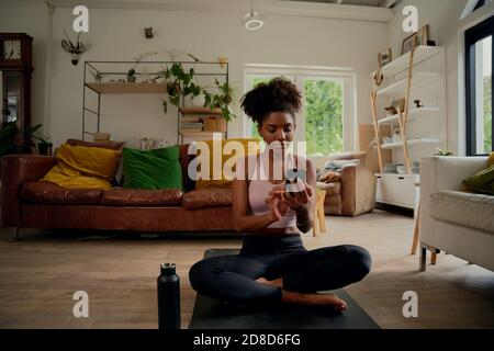 Porträt einer gesunden Frau, die zu Hause auf einer Yogamatte sitzt Smartphone wird überprüft Stockfoto