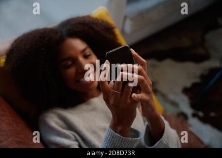 Nahaufnahme der hände afrikanischer Frau, die das Handy im Liegen halten Tisch Stockfoto