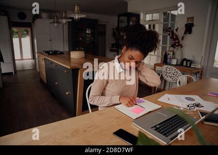 Afrikanische junge Frau leiden unter Nackenschmerzen arbeiten auf Laptop Mit Tagebuch und Dokument zu Hause Stockfoto