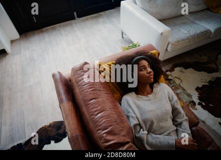 Deprimierte Frau mit Kopfhörern, die während der covid-19-Sperre auf der Couch liegen Wegschauen Stockfoto