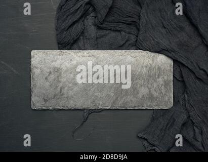 Unbeschriftete rechteckige Schieferplatte auf schwarzem Hintergrund und schwarze Textilserviette, Draufsicht Stockfoto