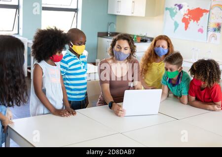 Weibliche Lehrerin trägt Gesichtsmaske mit Laptop, um Schüler zu lehren In der Klasse Stockfoto