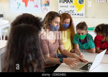 Weibliche Lehrerin trägt Gesichtsmaske mit Laptop, um Schüler zu lehren In der Klasse Stockfoto