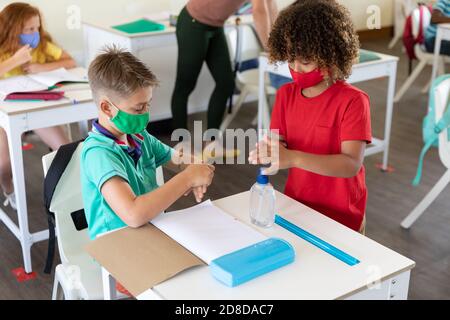 Zwei Jungen tragen Gesichtsmasken, die ihre Hände im Unterricht desinfizieren In der Schule Stockfoto