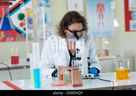 Lehrerin trägt Gesichtsmaske und Schutzbrille mit Mikroskop Im Labor Stockfoto