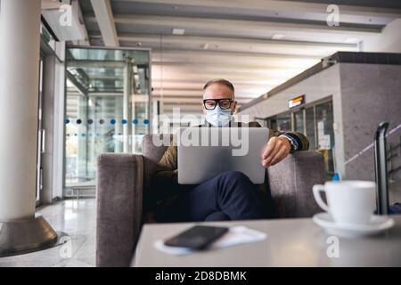 Geschäftsmann in einer Gesichtsmaske, die an seinem Laptop arbeitet Stockfoto