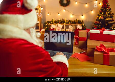 Blick von der Rückseite des Weihnachtsmannes, der an einem Tisch sitzt und einen Laptop für die Arbeit eindreht. Stockfoto