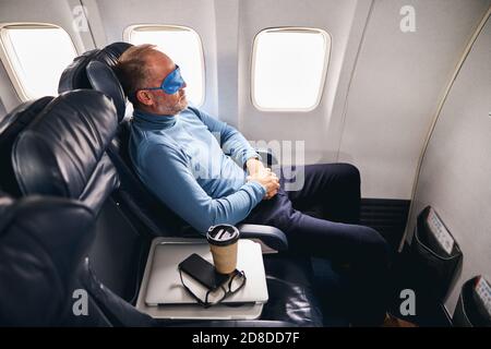 Mann in der Schlafmaske entspannt im Flugzeug Stockfoto