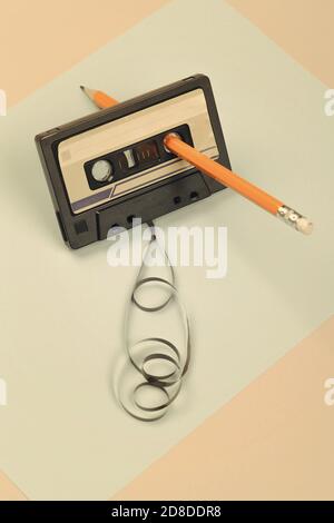 Audiokassette mit verworrenem Band auf blauem und beigem Hintergrund mit gelbem Bleistift, minimalistische Komposition. Retro-Konzept Stockfoto