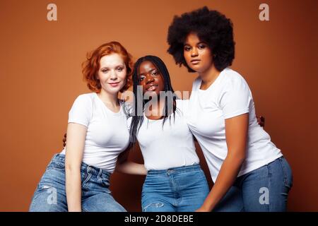 Junge hübsche kaukasische, afro, skandinavische Frau posiert fröhlich zusammen auf braunem Hintergrund, Lifestyle diverse Nationalität Menschen Konzept Stockfoto
