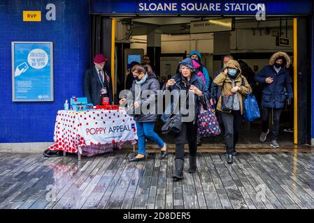 London, Großbritannien. Okt. 2020. Es ist der London Poppy Day und ein Veteran (in der Gruppe der Risikogruppen) der Luftlandetruppen, in seiner roten Baskenmütze, sammelt sich für die Royal British Legion, als ein stetiger Passagierstrom die U-Bahnstation Sloane Square verlässt. Er trägt eine Maske und Handschuhe und sammelt meist Geld mit kontaktlosen Zahlungen (obwohl er immer noch eine "Dose" für Bargeld hat). Reisende tragen meist Masken, nachdem sie obligatorisch geworden sind. Kredit: Guy Bell/Alamy Live Nachrichten Stockfoto