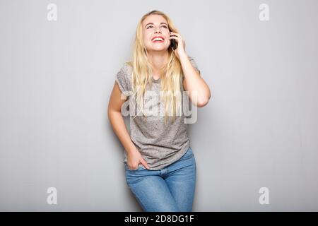 Porträt der coolen jungen blonden Frau lächeln und reden Mobiltelefon vor grauem Hintergrund Stockfoto