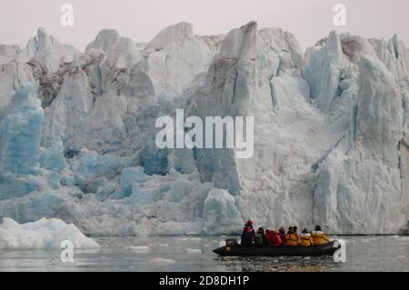 Touristen im Tierkreis segeln über die Mündung eines Gletschers in den hohen arktischen Gewässern. Stockfoto