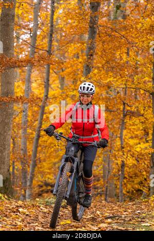 Sympathische aktive Seniorin, die mit ihrem Elektro-Mountainbike in den goldfarbenen Herbstwäldern der Schwäbischen Alb fährt Stockfoto