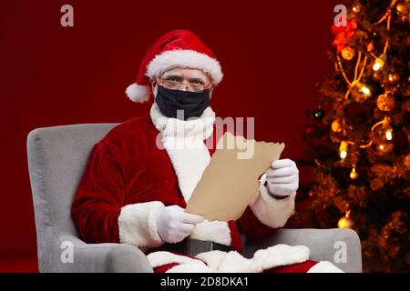 Porträt von Santa Claus trägt Schutzmaske Lesen eines Briefes Während Sie auf einem Sessel sitzen Stockfoto