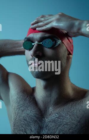 Nahaufnahme professionelle kaukasischen männlichen Schwimmer Vorbereitung für das Training isoliert auf blau neoned Studio Hintergrund. Anmut von Bewegung und Aktion. Gesundes Lifestyle-, Sport- und Bewegungskonzept. Stockfoto