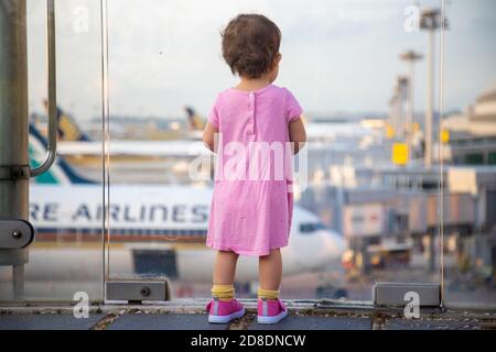 SINGAPUR - FEBRUAR 11 2020: Kleinkind in Pink Dress sieht sich Singapore Airlines geparkte Flugzeuge am Changi Airport an Stockfoto