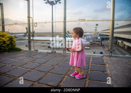 SINGAPUR - 11. FEBRUAR 2020: Kleinkind in einem rosa Kleid steht im Sonnenblumengarten auf dem Dach des Changi Airport vor der Kulisse Stockfoto