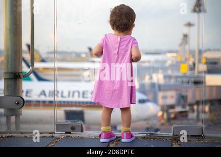 SINGAPUR - FEBRUAR 11 2020: Kleinkind in Pink Dress sieht sich Singapore Airlines geparkte Flugzeuge am Changi Airport an Stockfoto