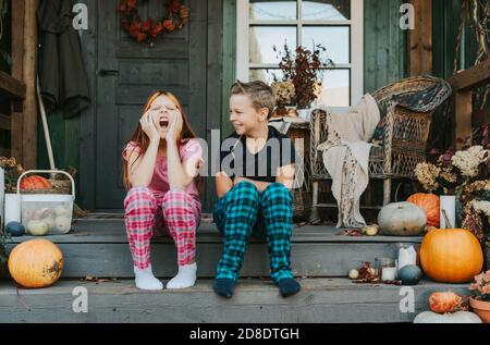 Kinder ein Junge und ein Mädchen im Pyjama sind gelangweilt Und Gähnen auf der Veranda des Hinterhofs mit eingerichtet Kürbisse im Herbst Stockfoto