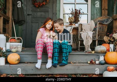 Kinder ein Junge und ein Mädchen im Pyjama mit ihren Hund, der Spaß auf der Veranda des Hinterhofs eingerichtet Mit Kürbissen im Herbst Stockfoto