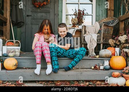 Kinder ein Junge und ein Mädchen im Pyjama mit ihren Hund, der Spaß auf der Veranda des Hinterhofs eingerichtet Mit Kürbissen im Herbst Stockfoto