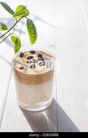 Traditionelles koreanisches Milchgetränk mit Koffein, Dalgona-Kaffee in einem transparenten Glas mit Kaffeebohnen auf einem Hintergrund aus weißen Brettern. Frühstück im a c Stockfoto
