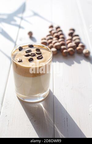 Traditionelles koreanisches koffeinhaltiges Milchgetränk, Dalgona-Kaffee in einem transparenten Glas mit Kaffeebohnen auf weißem Hintergrund. Frühstück in einem Café oder Stockfoto