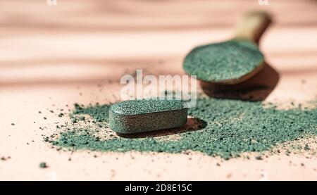 Nahaufnahme von Chlorella oder Spirulina Tabletten und Holzlöffel mit Pulver zwischen Pulver auf rosa Hintergrund in der Sonne Nahrungsergänzungsmittel, Detox Stockfoto