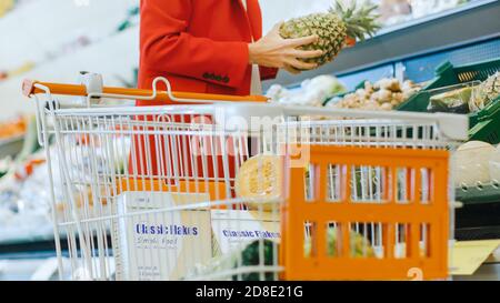 Im Supermarkt: Low Angle Shot der Frau, die Bio-Ananas aus der Frischeabteilung nimmt und in den Warenkorb legt. Stockfoto