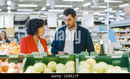 Im Supermarkt: Das glückliche junge Paar wählt Bio-Gemüse in der Frischwarenabteilung des Stores. Freund und Freundin abholen Stockfoto