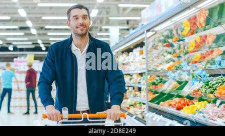 Im Supermarkt: Handsome Smiling man schiebt den Warenkorb, geht vorbei an Frischwaren Abschnitt des Geschäfts. Stockfoto