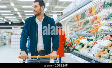 Im Supermarkt: Handsome Smiling man schiebt den Warenkorb, geht vorbei an Frischwaren Abschnitt des Geschäfts. Stockfoto